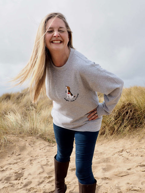 Ren Ellery wearing a beagles make me happy sweatshirt in grey, smiling, on Ainsdale Beach on a cold March afternoon.